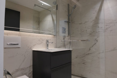 Inspiration for a medium sized contemporary grey and white shower room bathroom in Munich with flat-panel cabinets, grey cabinets, a corner shower, a wall mounted toilet, black and white tiles, stone tiles, white walls, a wall-mounted sink, white floors, an open shower, white worktops, a single sink and a floating vanity unit.