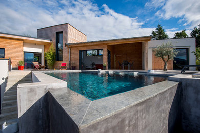 This is an example of a mid-sized contemporary backyard custom-shaped infinity pool in Grenoble with a pool house.