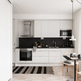 Создайте стильный интерьер: маленькая линейная кухня в скандинавском стиле с двойной раковиной, плоскими фасадами, белыми фасадами, черным фартуком, фартуком из сланца, техникой под мебельный фасад, светлым паркетным полом, бежевым полом, обеденным столом и черной столешницей без острова - последний тренд