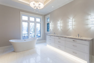 Large trendy master porcelain tile and white floor freestanding bathtub photo in Toronto with flat-panel cabinets, white cabinets, beige walls, an undermount sink and granite countertops