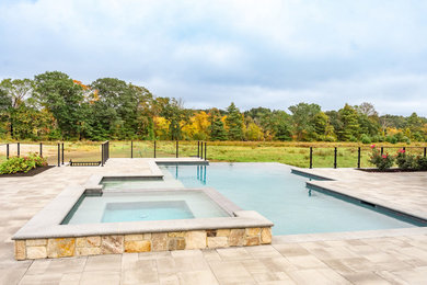 Ejemplo de piscina infinita actual grande a medida en patio trasero con adoquines de piedra natural
