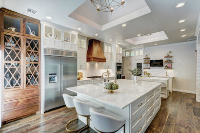 Inspiration for a large transitional open plan kitchen in Oklahoma City with a farmhouse sink, shaker cabinets, white cabinets, quartzite benchtops, white splashback, porcelain splashback, stainless steel appliances, medium hardwood floors, multiple islands and brown floor.