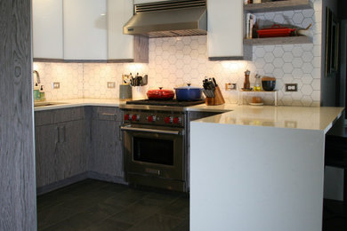 Inspiration for a mid-sized contemporary u-shaped porcelain tile, gray floor and vaulted ceiling eat-in kitchen remodel in New York with an undermount sink, glass-front cabinets, stainless steel cabinets, quartz countertops, white backsplash, ceramic backsplash, stainless steel appliances, a peninsula and white countertops