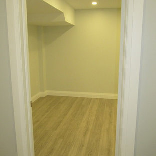 Modelo de sótano en el subsuelo moderno, grande, con paredes grises, suelo laminado, chimenea tradicional, marco de chimenea de baldosas y/o azulejos y suelo gris