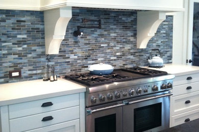 Mid-sized transitional galley dark wood floor and brown floor open concept kitchen photo in Los Angeles with recessed-panel cabinets, white cabinets, solid surface countertops, blue backsplash, mosaic tile backsplash, stainless steel appliances and an island