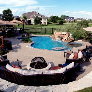 Free form pool with stone table, sun shelf, water feature, and outdoor kitchen,