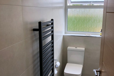 This is an example of a small modern grey and brown shower room bathroom in Dorset with flat-panel cabinets, grey cabinets, a corner shower, a two-piece toilet, grey tiles, ceramic tiles, grey walls, vinyl flooring, a wall-mounted sink, brown floors, a sliding door, a single sink and a floating vanity unit.