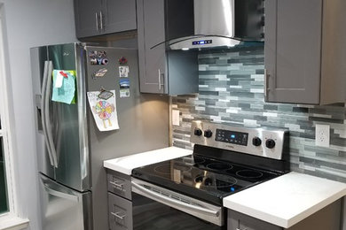 Inspiration for a mid-sized contemporary l-shaped porcelain tile and gray floor eat-in kitchen remodel in Houston with a farmhouse sink, shaker cabinets, gray cabinets, quartzite countertops, gray backsplash, glass sheet backsplash, stainless steel appliances, an island and white countertops
