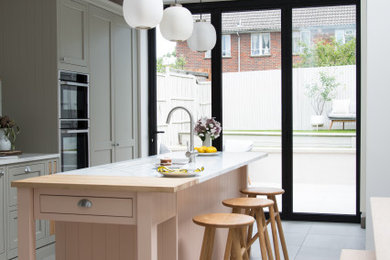 Inspiration for a contemporary eat-in kitchen in London with green cabinets, wood benchtops, white splashback, marble splashback, white appliances, white floor and white benchtop.