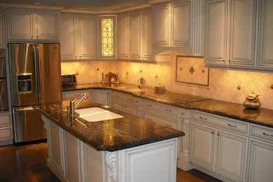 Kitchen pantry - large transitional kitchen pantry idea in Orange County with an undermount sink, raised-panel cabinets, white cabinets, granite countertops, beige backsplash, stone tile backsplash, stainless steel appliances and an island