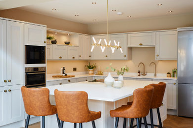 Design ideas for a traditional kitchen in Other with an integrated sink, shaker cabinets, beige cabinets, marble worktops, white splashback, stainless steel appliances, medium hardwood flooring, an island, brown floors and white worktops.