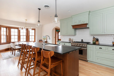 Example of a large arts and crafts l-shaped medium tone wood floor and brown floor eat-in kitchen design in Other with an undermount sink, recessed-panel cabinets, green cabinets, quartz countertops, white backsplash, marble backsplash, an island and black countertops