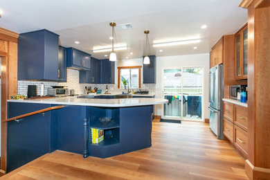 Elegant medium tone wood floor kitchen photo in Los Angeles with a farmhouse sink, shaker cabinets, blue cabinets, quartz countertops, porcelain backsplash and a peninsula