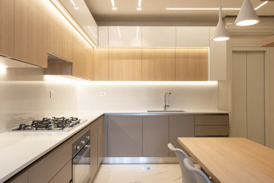 Large modern grey and cream l-shaped kitchen in London with grey cabinets, white splashback, stone slab splashback, stainless steel appliances, marble flooring, a breakfast bar, white worktops, a drop ceiling and feature lighting.