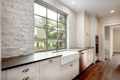 Large arts and crafts l-shaped medium tone wood floor kitchen photo in Boston with a farmhouse sink, recessed-panel cabinets, white cabinets, solid surface countertops, white backsplash, stone tile backsplash, stainless steel appliances and an island