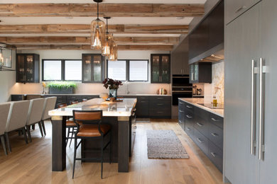 Example of a huge urban l-shaped light wood floor, brown floor and exposed beam eat-in kitchen design in Minneapolis with a drop-in sink, flat-panel cabinets, dark wood cabinets, marble countertops, white backsplash, stone slab backsplash, stainless steel appliances, an island and white countertops