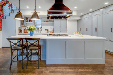 Example of a tuscan medium tone wood floor and brown floor kitchen design in New York with a farmhouse sink, shaker cabinets, gray cabinets, quartz countertops, black appliances, an island and white countertops