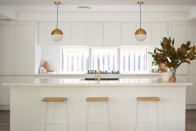 Photo of a large contemporary galley eat-in kitchen in Sydney with a farmhouse sink, white cabinets, quartz benchtops, white splashback, mosaic tile splashback, black appliances, light hardwood floors, with island, beige floor and white benchtop.