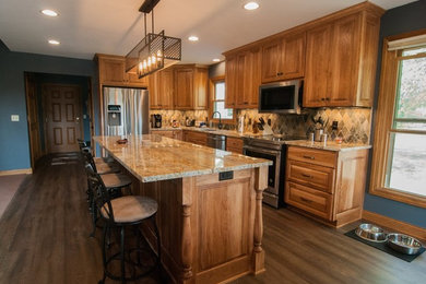 Example of a mid-sized classic l-shaped dark wood floor and brown floor kitchen pantry design in Milwaukee with an undermount sink, recessed-panel cabinets, medium tone wood cabinets, granite countertops, multicolored backsplash, terra-cotta backsplash, stainless steel appliances and an island