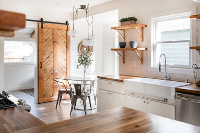 Example of a small country u-shaped laminate floor and gray floor kitchen design in Phoenix with a farmhouse sink, shaker cabinets, white cabinets, wood countertops, stainless steel appliances, white backsplash, subway tile backsplash and brown countertops