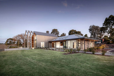 Large modern two-storey grey house exterior in Melbourne with metal siding, a gable roof, a metal roof and a grey roof.