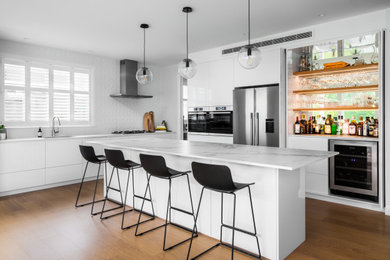 This is an example of a large contemporary l-shaped eat-in kitchen in Auckland with an undermount sink, recessed-panel cabinets, white cabinets, quartz benchtops, white splashback, porcelain splashback, stainless steel appliances, light hardwood floors, with island and yellow benchtop.