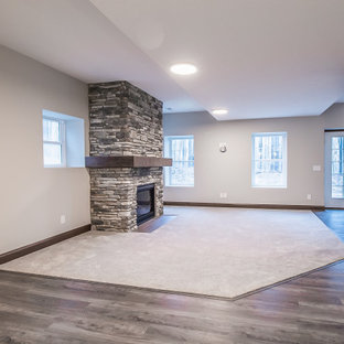 Idée de décoration pour un très grand sous-sol tradition donnant sur l'extérieur avec un mur gris, un sol en bois clair, une cheminée standard, un manteau de cheminée en pierre de parement et un sol multicolore.