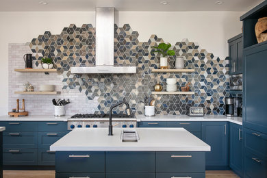 Inspiration for a beach style l-shaped kitchen in Other with an undermount sink, shaker cabinets, blue cabinets, multi-coloured splashback, stainless steel appliances, light hardwood floors, with island and white benchtop.