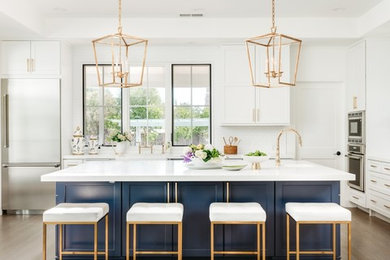 Transitional medium tone wood floor and brown floor kitchen photo in Miami with shaker cabinets, white cabinets, white backsplash, stainless steel appliances, an island and white countertops