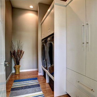 This is an example of a small contemporary single-wall separated utility room in Grand Rapids with flat-panel cabinets, white cabinets, grey walls, bamboo flooring and a side by side washer and dryer.