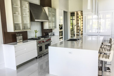 Example of a mid-sized minimalist l-shaped porcelain tile and white floor open concept kitchen design in Miami with solid surface countertops, an undermount sink, flat-panel cabinets, white cabinets, brown backsplash, stone slab backsplash, stainless steel appliances, an island and white countertops
