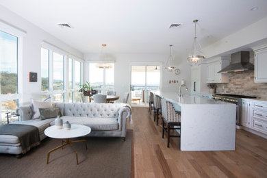 Mid-sized elegant galley light wood floor and multicolored floor open concept kitchen photo in Other with a farmhouse sink, raised-panel cabinets, white cabinets, quartzite countertops, beige backsplash, ceramic backsplash, stainless steel appliances, an island and white countertops