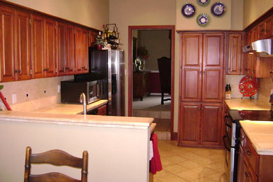 Mid-sized trendy u-shaped porcelain tile kitchen photo in Austin with a drop-in sink, raised-panel cabinets, medium tone wood cabinets, tile countertops, beige backsplash, stone tile backsplash, stainless steel appliances and a peninsula