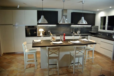 Réalisation d'une grande cuisine américaine design en L avec un évier 1 bac, un placard à porte affleurante, des portes de placard blanches, un plan de travail en stratifié, un électroménager en acier inoxydable, tomettes au sol, îlot, un sol orange et plan de travail noir.