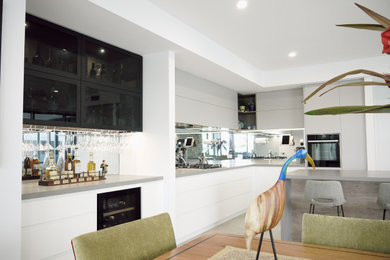 Inspiration for a large modern l-shaped eat-in kitchen in Sunshine Coast with a double-bowl sink, white cabinets, quartz benchtops, mirror splashback, stainless steel appliances, with island and grey benchtop.