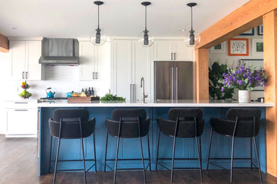 Example of a huge cottage galley vinyl floor, brown floor and exposed beam open concept kitchen design in San Diego with a farmhouse sink, shaker cabinets, blue cabinets, quartzite countertops, white backsplash, porcelain backsplash, stainless steel appliances, an island and white countertops