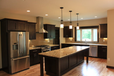 Example of a large arts and crafts l-shaped medium tone wood floor and brown floor kitchen design in Cedar Rapids with an undermount sink, shaker cabinets, dark wood cabinets, granite countertops, beige backsplash, subway tile backsplash, stainless steel appliances and an island