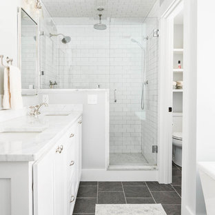 Cette image montre une salle de bain principale traditionnelle de taille moyenne avec un placard à porte shaker, des portes de placard blanches, une baignoire indépendante, une douche ouverte, un carrelage blanc, un carrelage métro, un mur gris, un sol en ardoise, un lavabo encastré, un plan de toilette en marbre, un sol gris et une cabine de douche à porte battante.