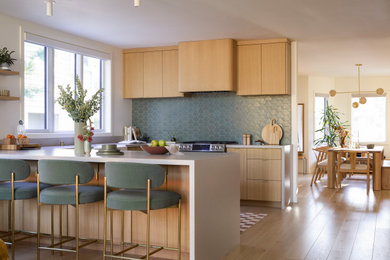 Mid-sized trendy light wood floor and beige floor open concept kitchen photo in San Francisco with a farmhouse sink, flat-panel cabinets, light wood cabinets, quartz countertops, green backsplash, ceramic backsplash, stainless steel appliances, a peninsula and gray countertops