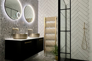 This is an example of a medium sized urban grey and black shower room bathroom in London with flat-panel cabinets, black cabinets, a walk-in shower, a wall mounted toilet, beige tiles, porcelain tiles, grey walls, terrazzo flooring, a console sink, solid surface worktops, grey floors, an open shower, white worktops, an enclosed toilet, double sinks and a floating vanity unit.