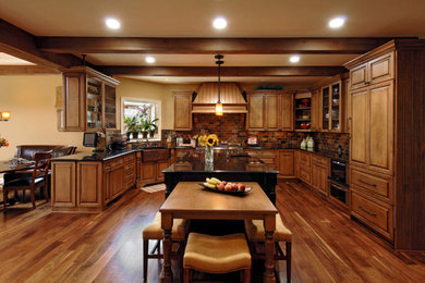 Example of a large classic u-shaped dark wood floor and brown floor eat-in kitchen design in Orange County with a farmhouse sink, raised-panel cabinets, medium tone wood cabinets, granite countertops, red backsplash, brick backsplash, paneled appliances, an island and black countertops