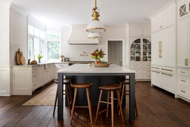 Kitchen - traditional u-shaped dark wood floor and brown floor kitchen idea in Seattle with a farmhouse sink, recessed-panel cabinets, white cabinets, white backsplash, subway tile backsplash, an island, white countertops and paneled appliances
