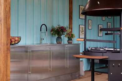Imagen de cocina industrial con armarios con paneles lisos, puertas de armario en acero inoxidable y encimera de acero inoxidable