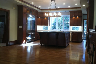 Large elegant light wood floor open concept kitchen photo in San Francisco with a farmhouse sink, shaker cabinets, dark wood cabinets, quartz countertops, white backsplash, ceramic backsplash, stainless steel appliances and an island
