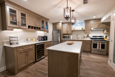 Mid-sized transitional l-shaped enclosed kitchen photo in Other with a double-bowl sink, shaker cabinets, brown cabinets, quartz countertops, white backsplash, quartz backsplash, stainless steel appliances, an island and white countertops