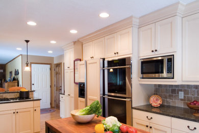 Example of a mid-sized transitional u-shaped medium tone wood floor and brown floor open concept kitchen design in Columbus with a farmhouse sink, recessed-panel cabinets, white cabinets, granite countertops, beige backsplash, stone tile backsplash, stainless steel appliances and a peninsula