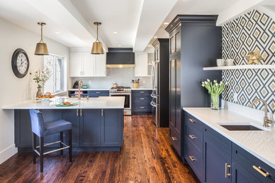 Inspiration for a mid-sized transitional l-shaped open plan kitchen in Vancouver with a farmhouse sink, shaker cabinets, blue cabinets, quartz benchtops, grey splashback, subway tile splashback, stainless steel appliances, medium hardwood floors, a peninsula and brown floor.