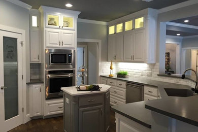 Inspiration for a mid-sized transitional u-shaped dark wood floor kitchen remodel in Austin with an undermount sink, raised-panel cabinets, white cabinets, solid surface countertops, white backsplash, subway tile backsplash, stainless steel appliances and an island