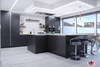 This is an example of a modern kitchen in London with black cabinets, white splashback, stainless steel appliances, with island and white benchtop.
