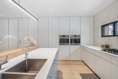 Example of a large minimalist u-shaped medium tone wood floor and beige floor open concept kitchen design in Toronto with an undermount sink, flat-panel cabinets, white cabinets, quartz countertops, red backsplash, porcelain backsplash, paneled appliances, an island and turquoise countertops